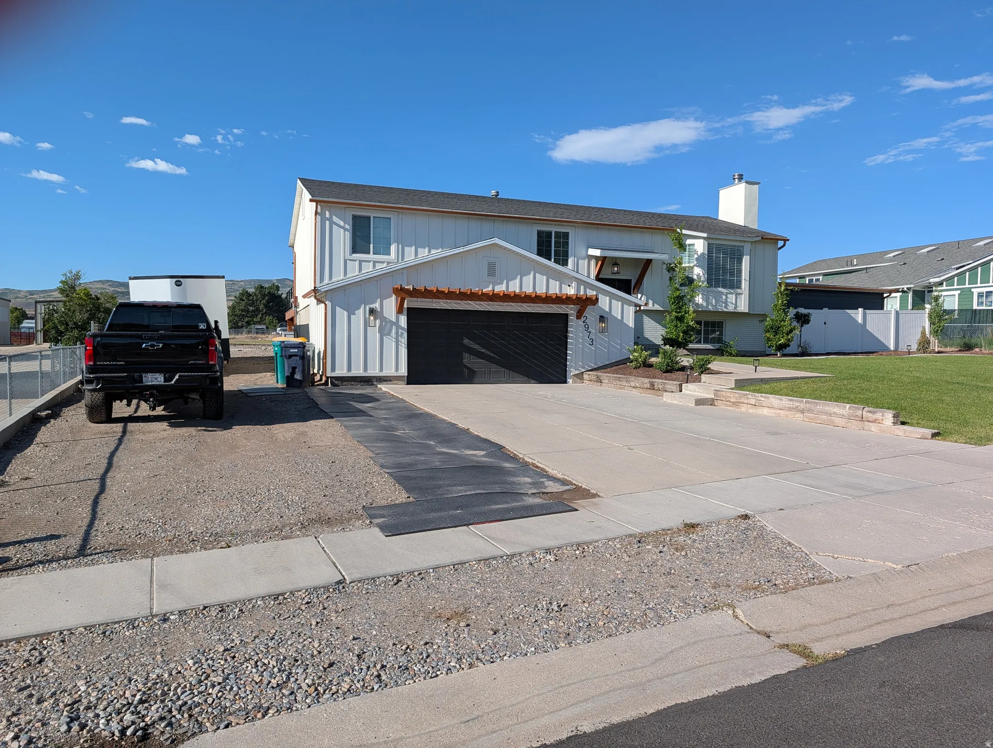 Split-level residence featuring white vertical siding and a two-car garage with a black door