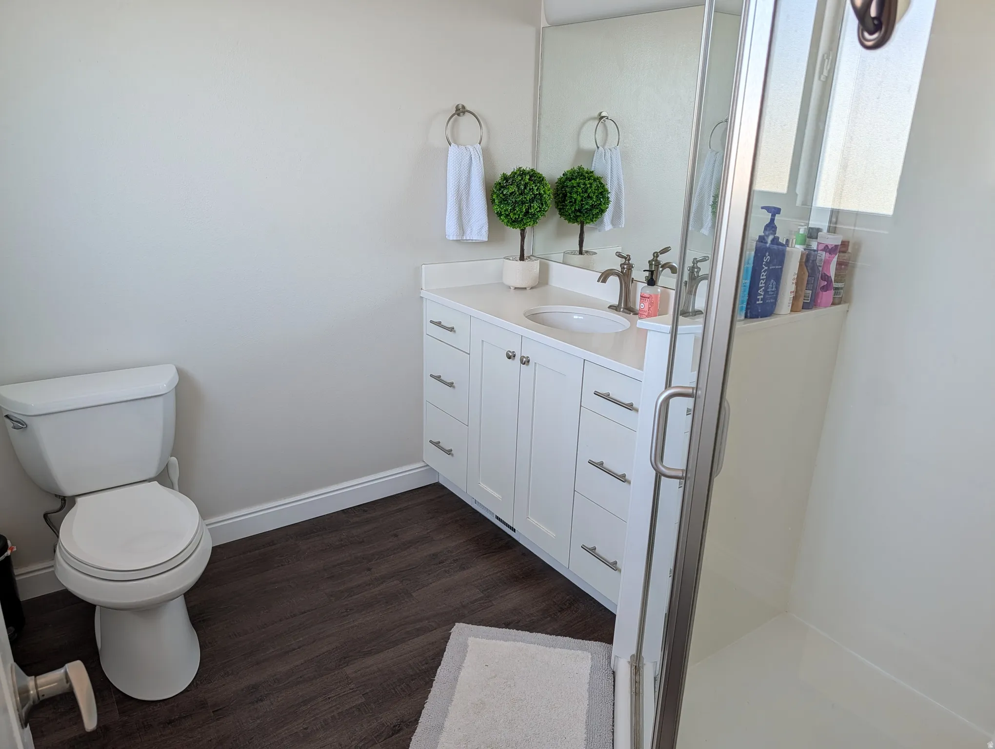 Bathroom featuring a glass-enclosed shower, a white vanity with an integrated sink, a white countertop, and wood-finish flooring