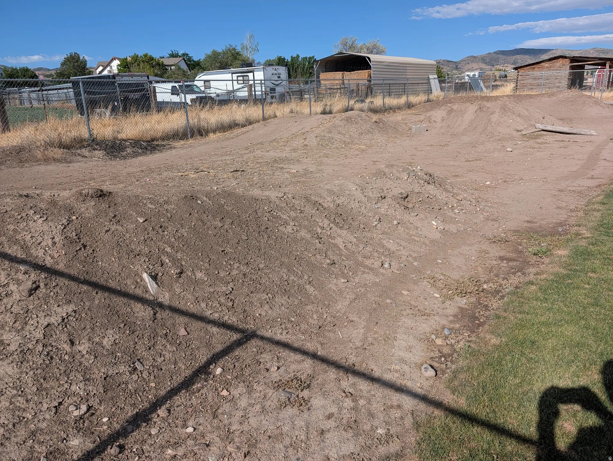 Dirt bike track. Expansive dirt area featuring multiple earthen mounds and a partial chain-link fence boundary