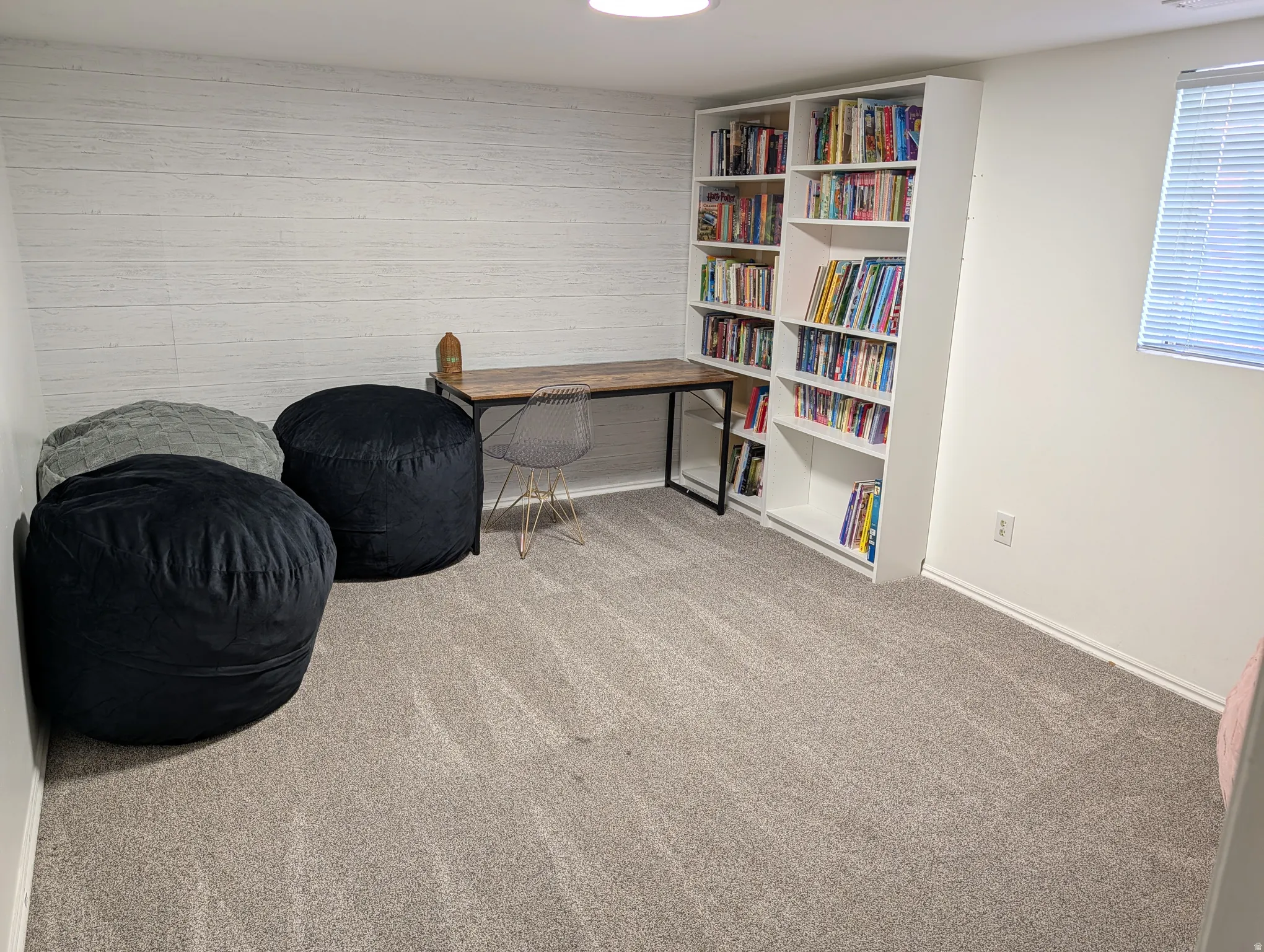 Spacious room featuring light gray carpet flooring, a white textured accent wall, and built-in white shelving