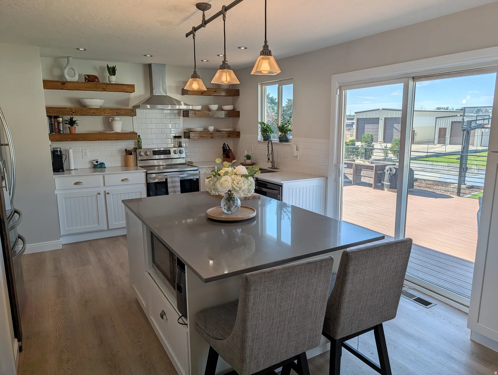 Contemporary kitchen featuring an oversized island with countertop seating, stainless steel appliances, a white subway tile backsplash, and open wood shelving