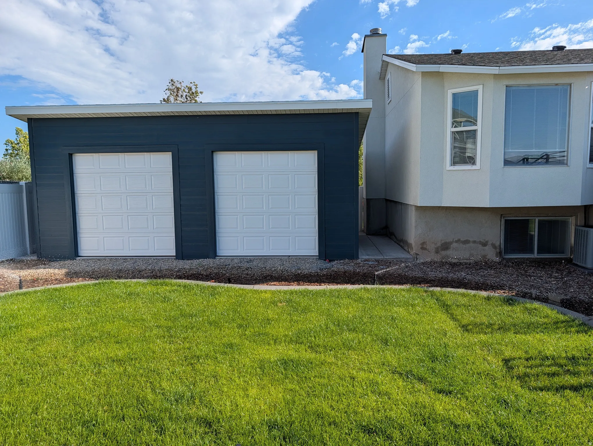 Detached two-car garage with dark blue horizontal siding and white panel garage doors