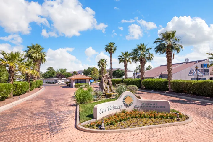 Entryway featuring a patterned paver driveway, mature palm trees, sculpted hedges, a stone water feature, and a signage monument