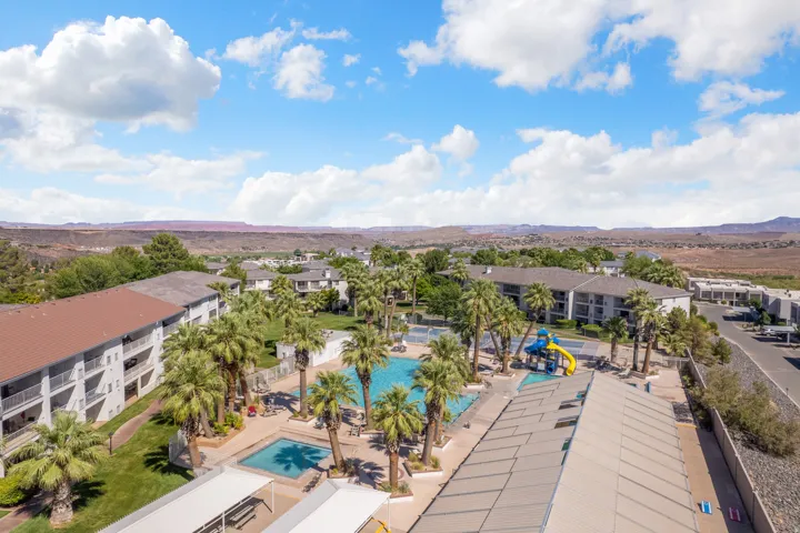 Community pool area featuring multiple swimming pools, mature palm trees, a vibrant playground structure, ample lounge seating, and covered patio areas