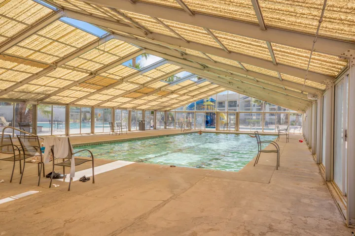 Enclosed pool facility featuring a translucent, gabled roof with skylights, surrounded by full-height glass panels