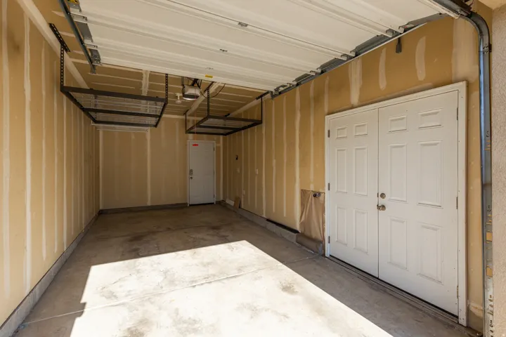 Garage interior featuring a concrete floor, exposed wall studs, an overhead garage door, and two white paneled doors