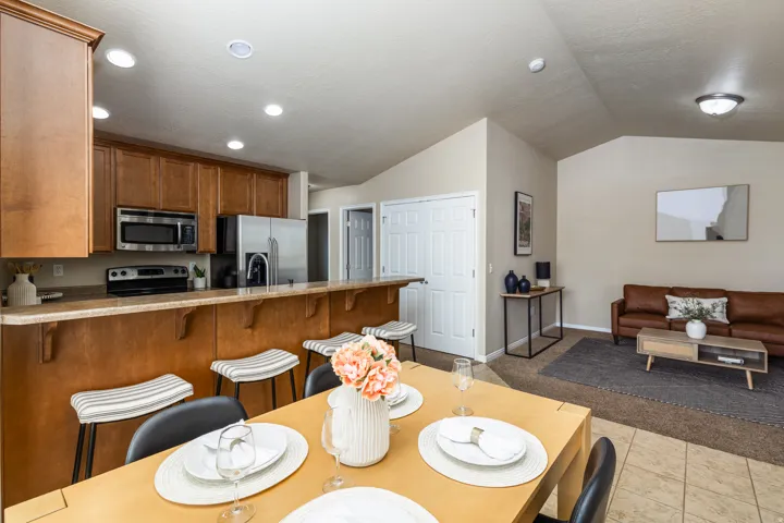 Open-concept living area featuring a kitchen with wood cabinetry and stainless steel appliances, a breakfast bar, a dining area with tile flooring, and a carpeted lounge space with vaulted ceilings