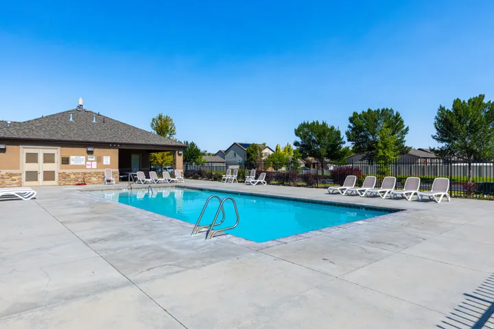 Outdoor swimming pool with concrete surround, featuring a nearby pool house with a covered patio area, and perimeter fencing