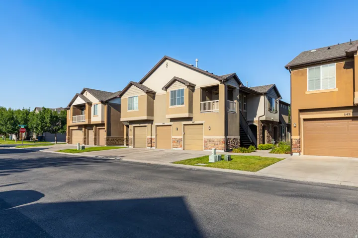 Residential buildings featuring stucco and stone veneer exteriors, attached garages with brown doors, and private balconies with white railings