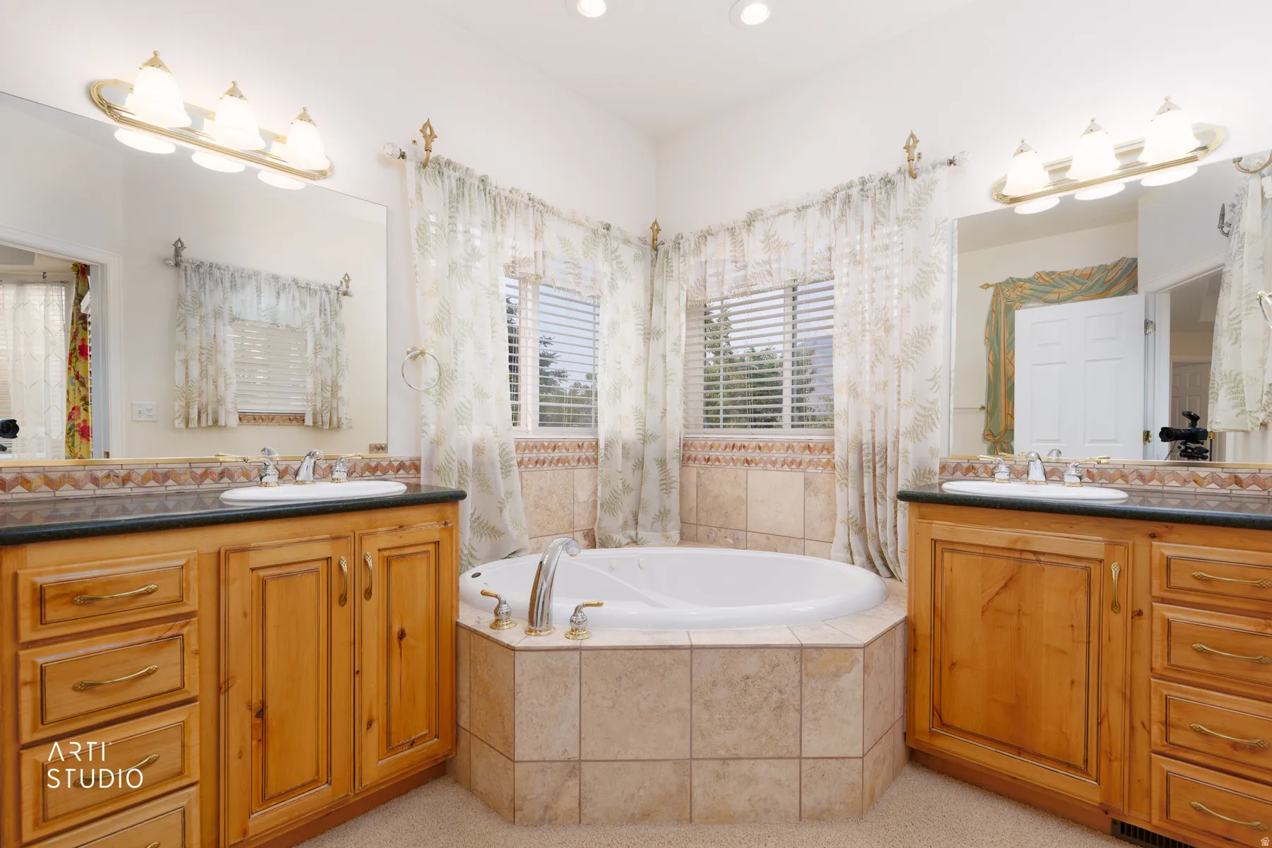 Spacious Master bathroom featuring a built-in jetted tub surrounded by tile, two wood-finish vanities with dark countertops and integrated sinks, and overhead vanity lighting