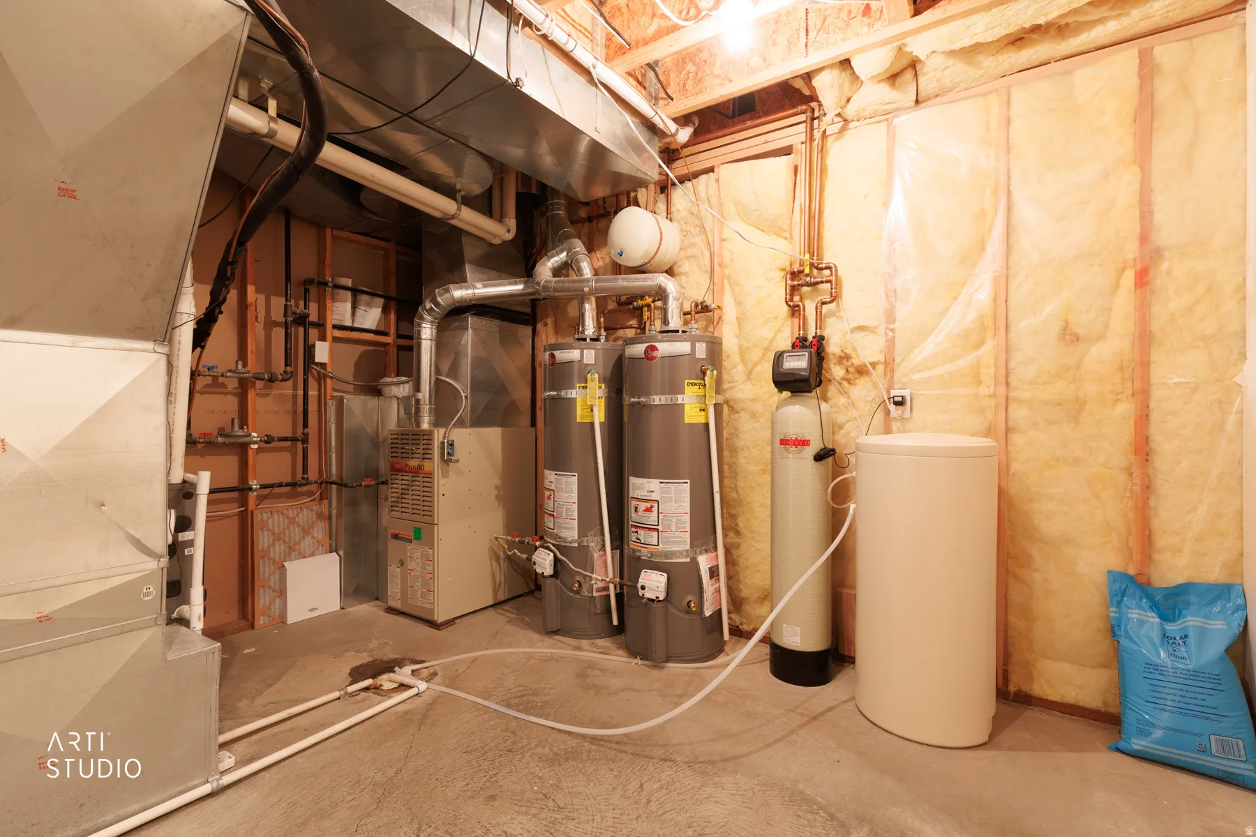 Dedicated utility space featuring two water heaters, a forced-air furnace, a water softener system, and exposed insulation