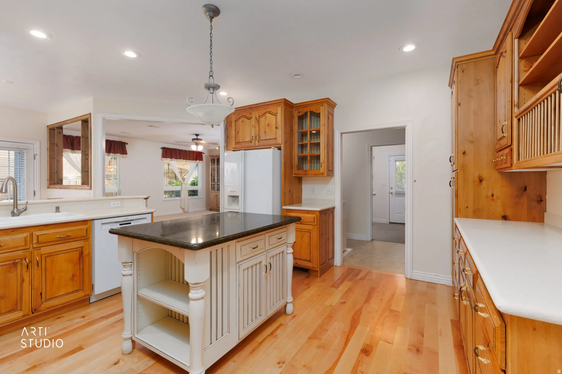 Kitchen featuring a central island with a dark countertop and decorative legs, hardwood flooring, natural wood-finish cabinetry, recessed lighting, and a double basin sink with a gooseneck faucet
