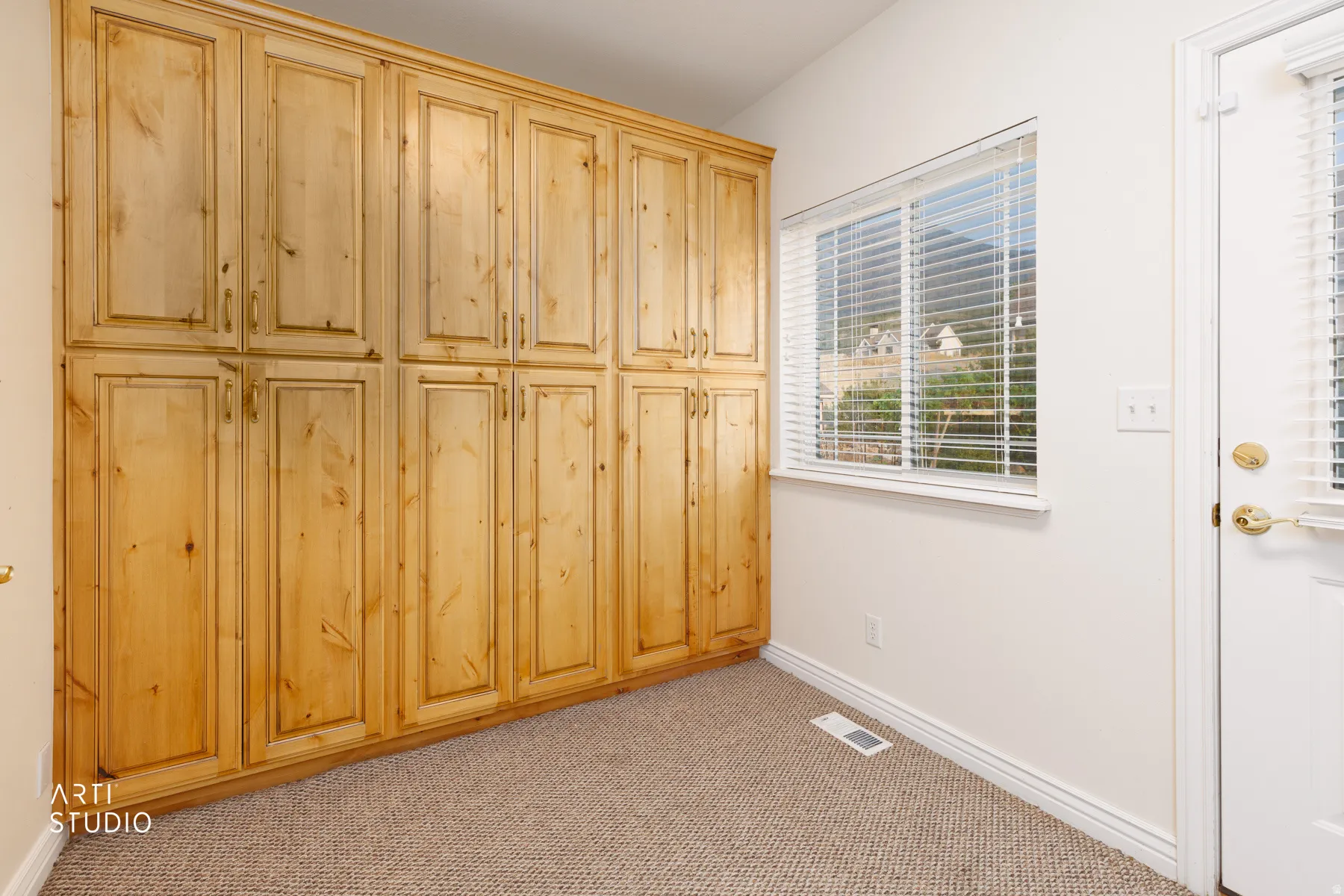 Extensive built-in wood cabinetry with brass hardware in the mudroom, complemented by a window with blinds and a white exterior door