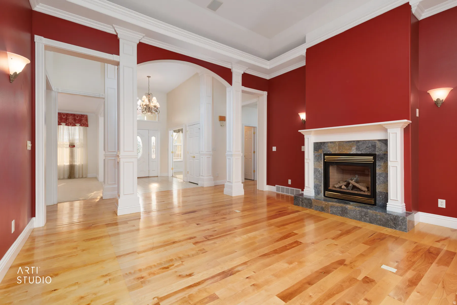 Spacious living area featuring wood-finish flooring, a stone-surround fireplace with white mantel, wall sconces, and extensive white crown molding