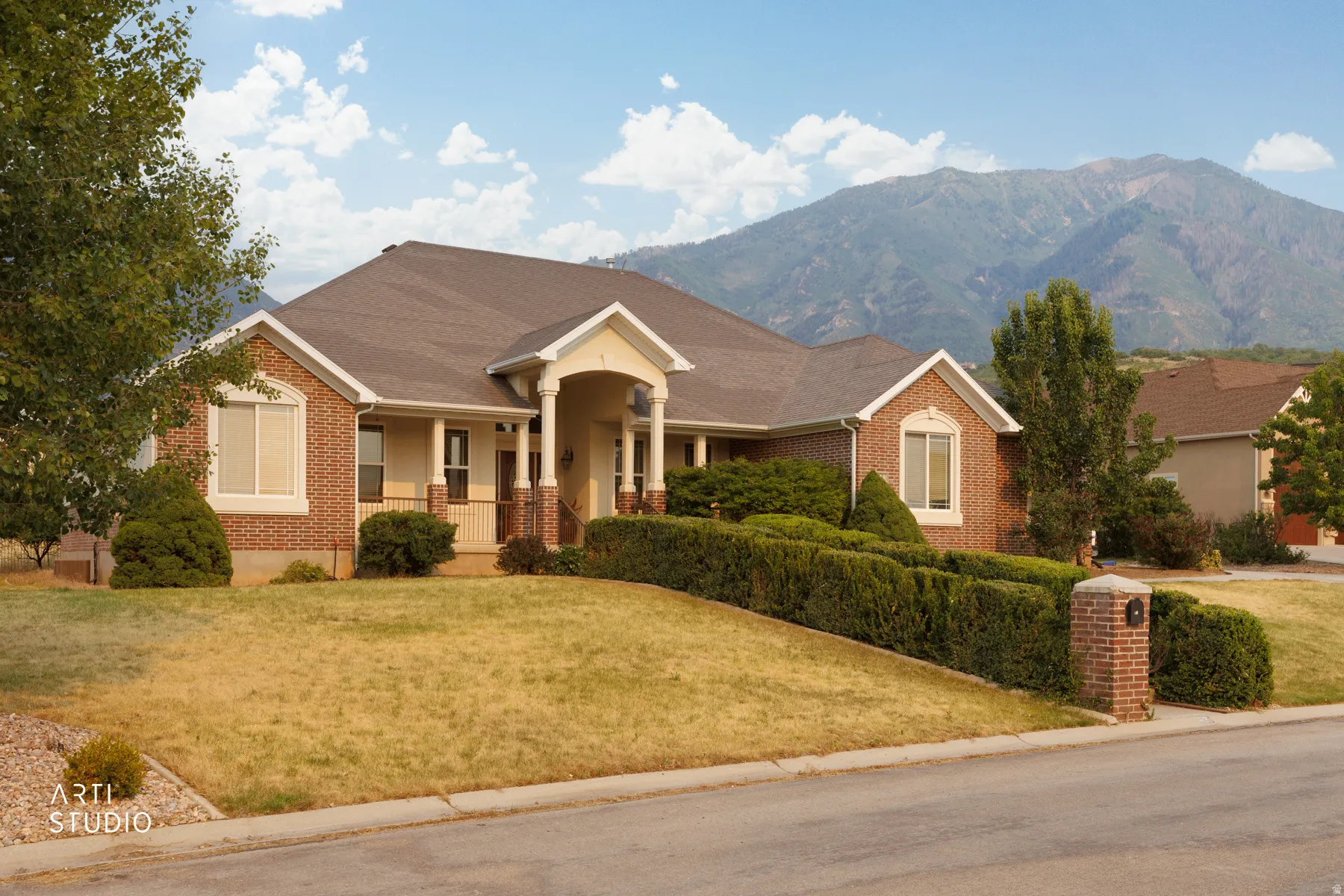 Brick exterior residence with a columned front entry, mature landscaping, and an integrated two-car garage