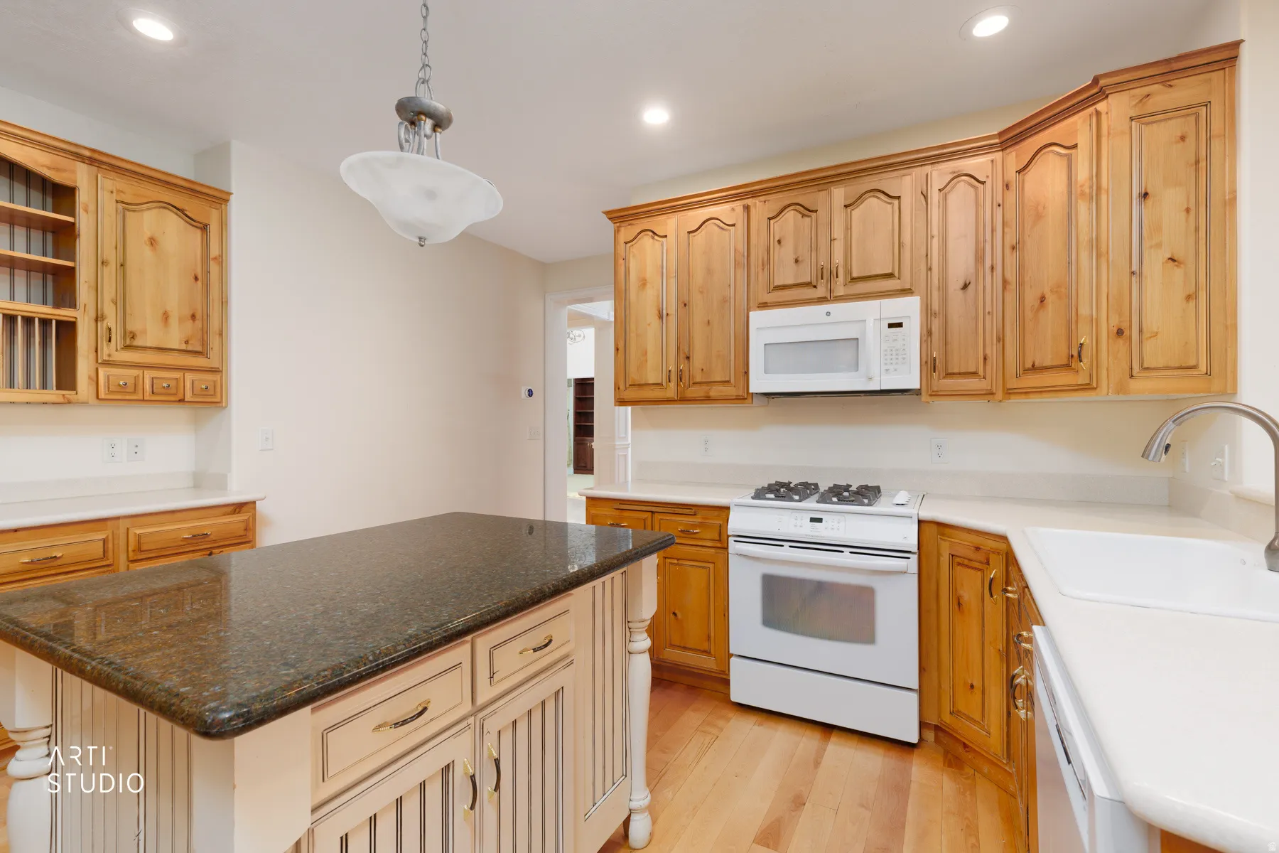 Kitchen featuring light wood cabinetry, a central island with a dark stone-finish countertop, white countertops, a white gas range, and a white microwave