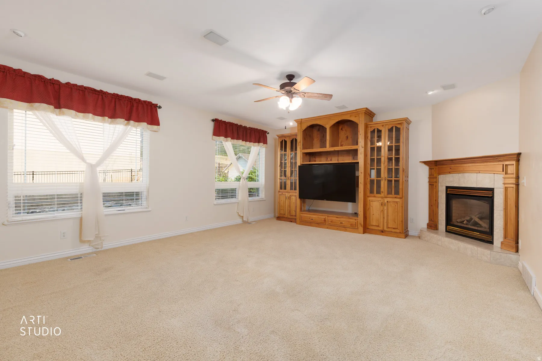 Spacious room featuring a corner fireplace with a tile surround and wood mantel, a built-in entertainment center with glass-front cabinetry, neutral carpeting, and multiple windows