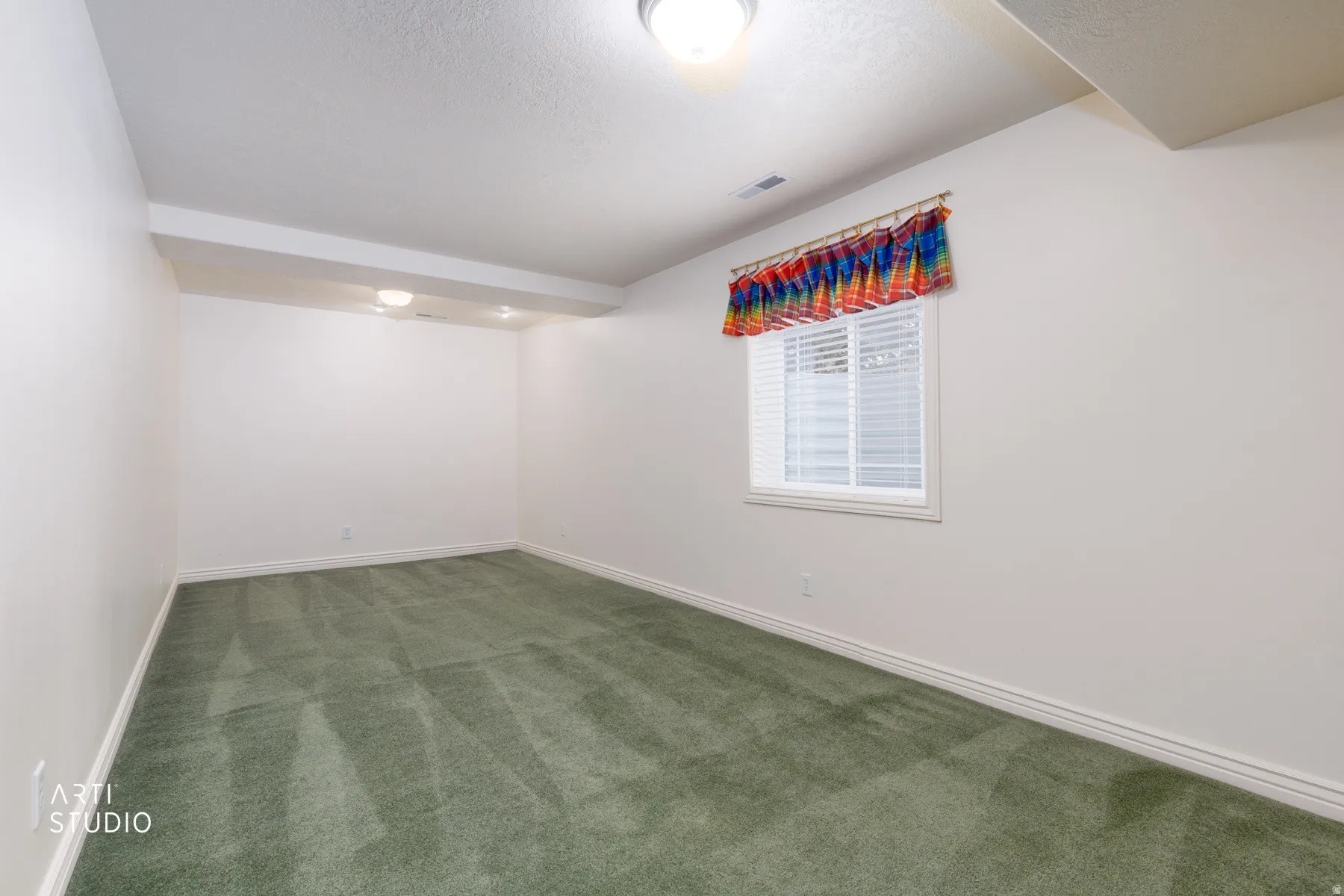 Spacious room featuring green carpet flooring, white painted walls, and a window with horizontal blinds