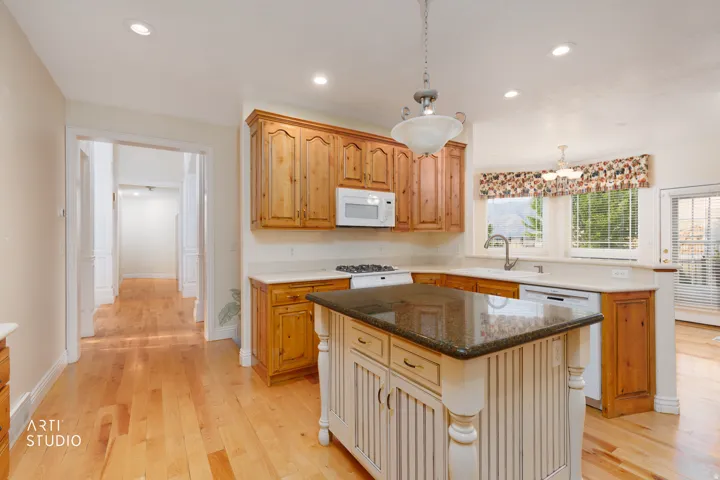 Kitchen featuring light wood-finish flooring, a central island with a dark countertop, perimeter white countertops, natural wood cabinetry, and recessed lighting