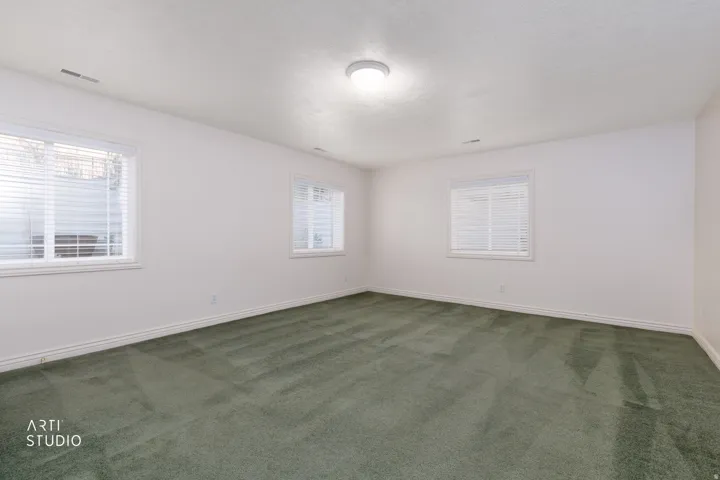 Spacious interior room featuring plush green carpeting and multiple windows with white blinds