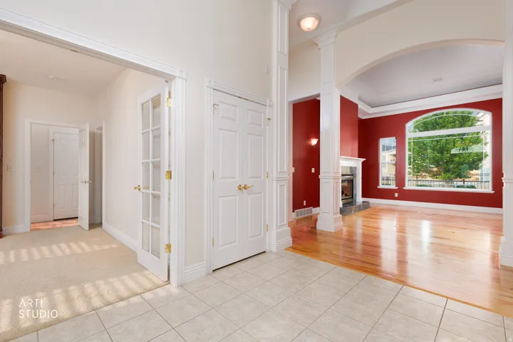 Entryway featuring ceramic tile flooring, leading to a living area with hardwood flooring, a fireplace with a white mantel, and large arched windows