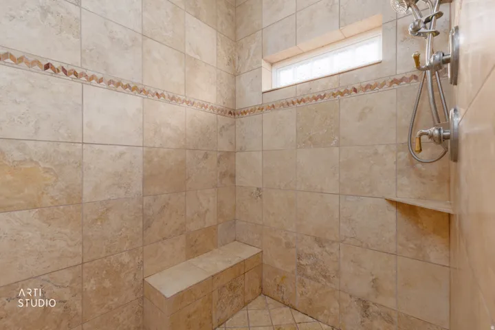 Neutral-toned tile shower featuring a built-in bench, mosaic accent tile, and a multi-function showerhead