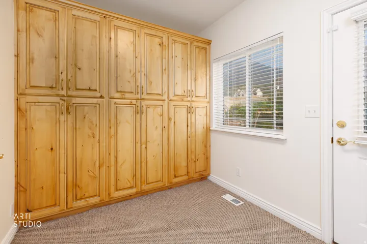 Extensive built-in wood cabinetry with brass hardware in the mudroom, complemented by a window with blinds and a white exterior door