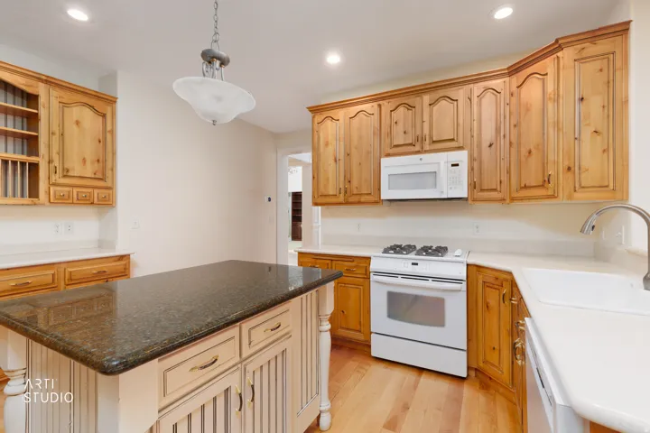 Kitchen featuring light wood cabinetry, a central island with a dark stone-finish countertop, white countertops, a white gas range, and a white microwave