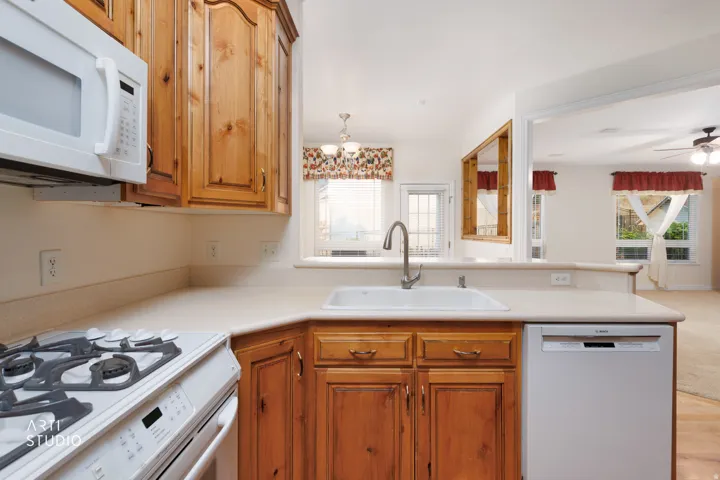 Kitchen featuring wood cabinetry, solid surface countertops, an undermount sink with a gooseneck faucet, an over-the-range microwave, and a gas range