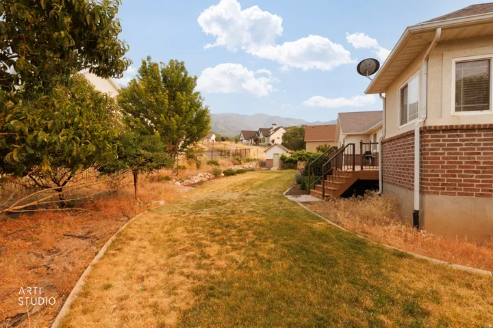 Expansive backyard space with a sloped grade, featuring mature trees and a concrete border