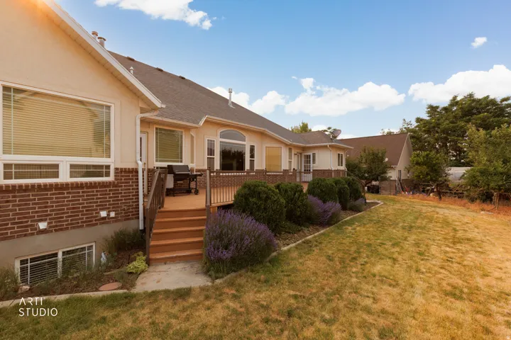 Rear exterior featuring a multi-level wood deck with railings, brick and stucco siding, mature landscaping, and a sloped lawn