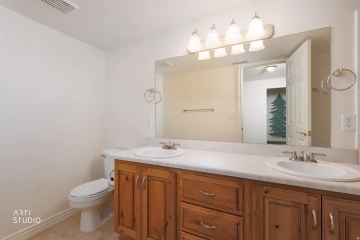 Bathroom vanity featuring dual drop-in sinks, a light-toned countertop, and natural wood cabinetry with brushed nickel hardware
