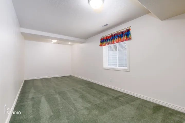 Spacious room featuring green carpet flooring, white painted walls, and a window with horizontal blinds