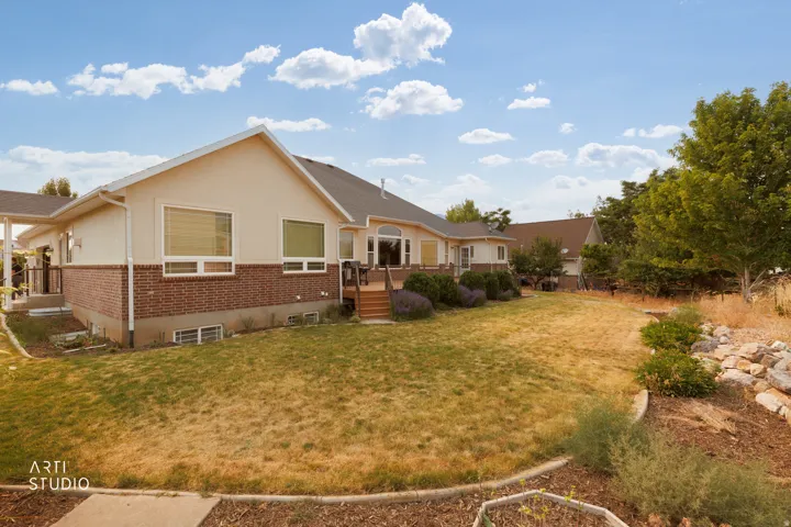 Rear exterior featuring a brick and stucco facade, multiple windows, a wooden deck with stairs, a patio, and mature landscaping