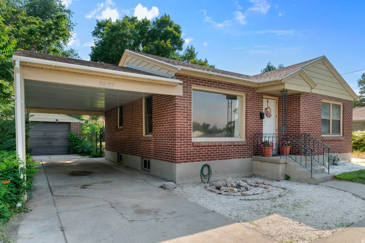 Brick exterior featuring a covered carport, a separate detached garage, and a large front picture window