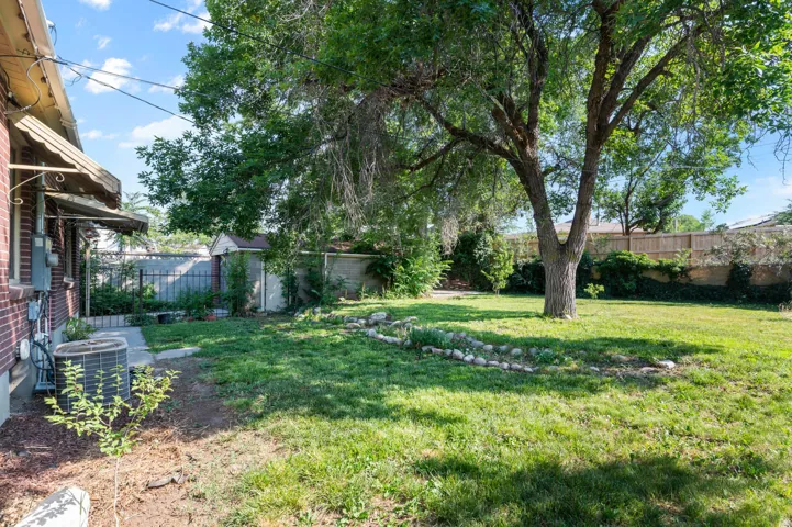 Expansive rear yard featuring mature trees, green lawn, a dedicated garden area, brick exterior siding, and an outdoor storage shed