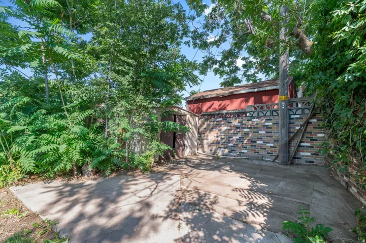 Concrete paved area bordered by mature foliage and a multi-toned brick wall
