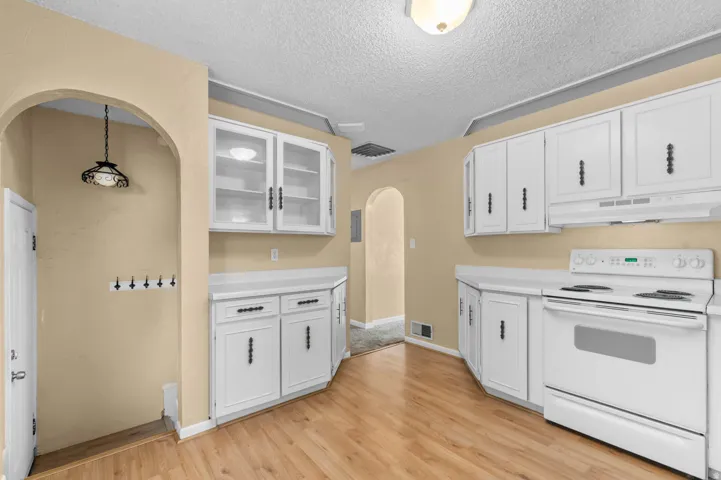 Kitchen featuring wood-finish flooring, white cabinetry with dark hardware, white countertops, a white electric range, and a white range hood