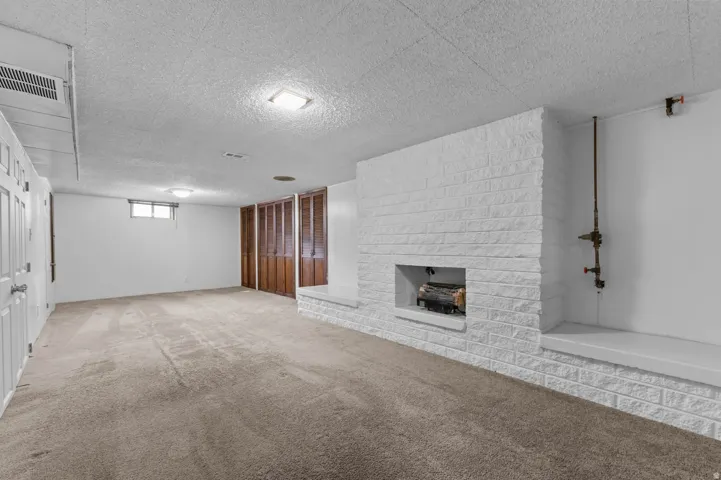 Expansive room featuring a prominent white brick fireplace with a built-in hearth, textured ceiling, brown wood-finish bifold doors, and neutral carpeting
