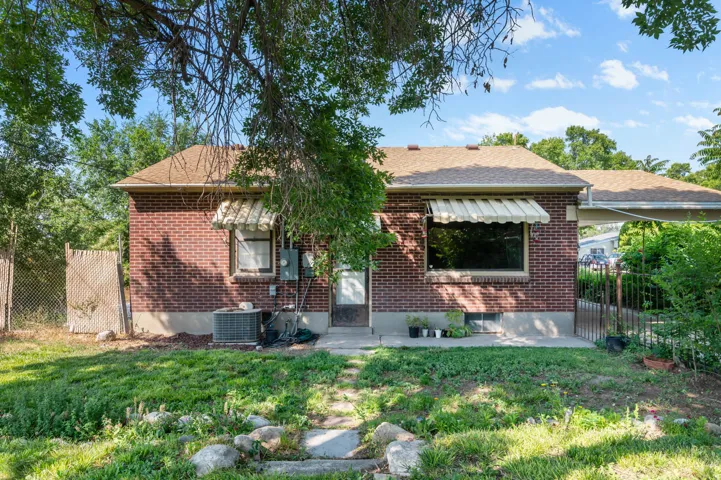Brick exterior featuring a brown shingle roof, two windows with striped awnings, and a concrete patio