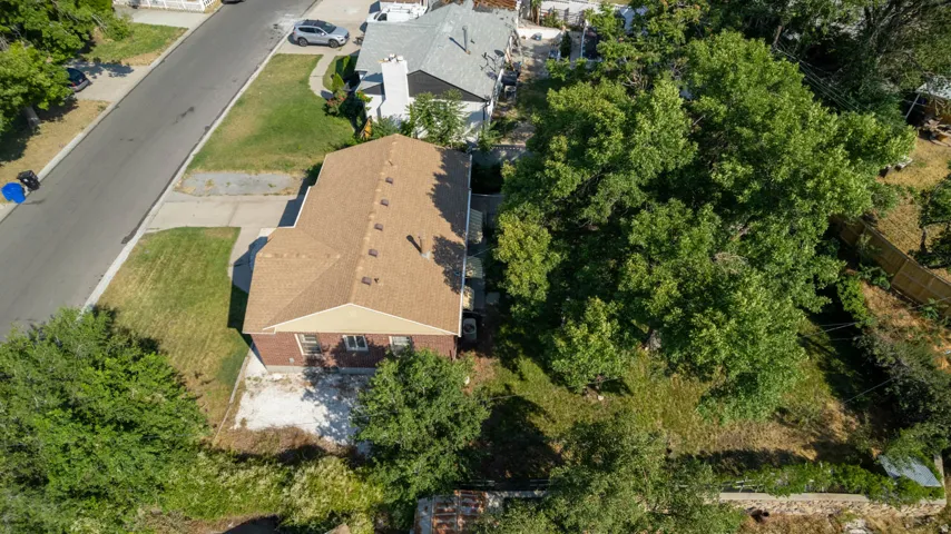 Brick exterior with a brown shingled roof, featuring a paved driveway and an expansive rear yard with mature trees