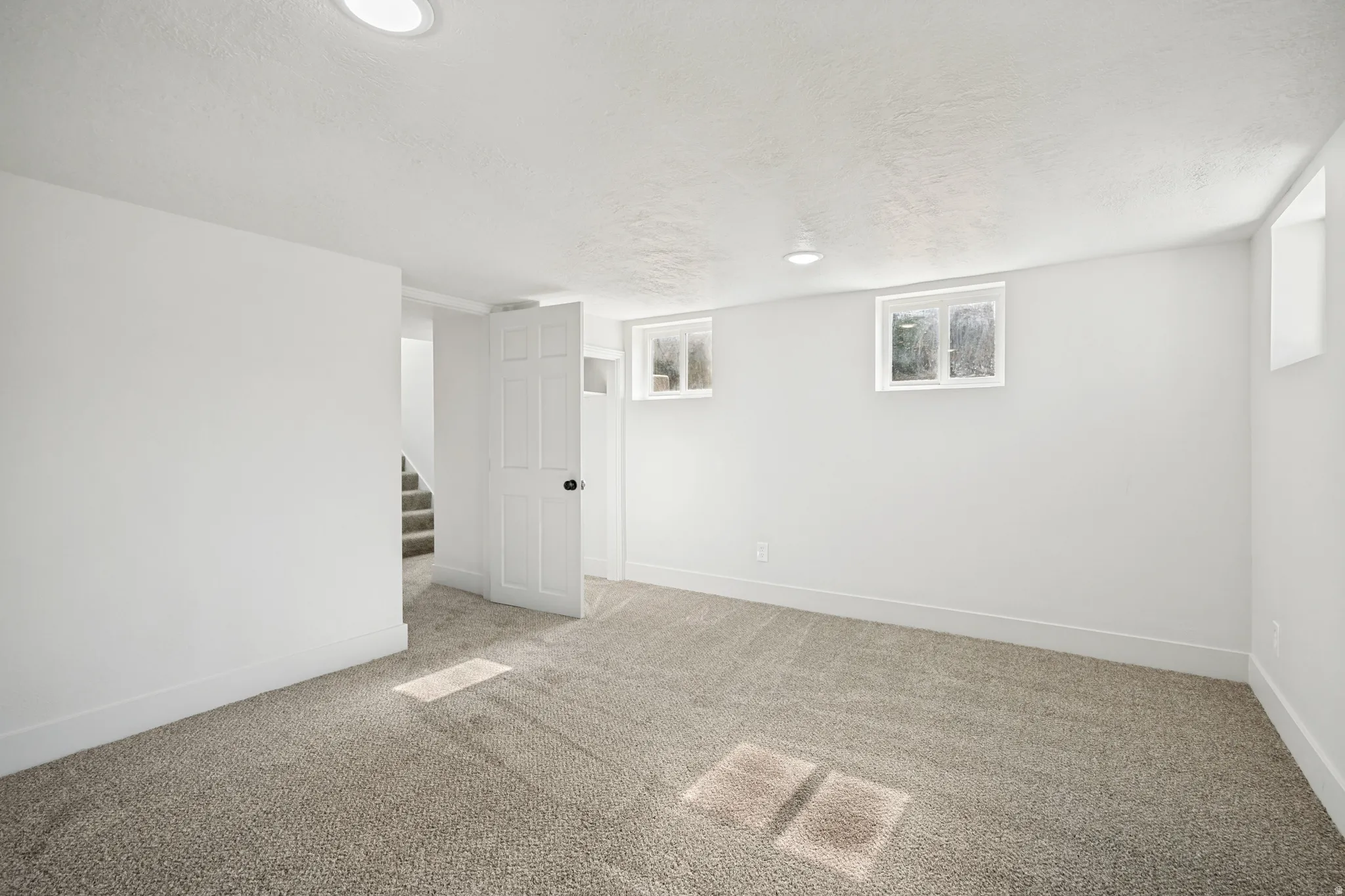 Spacious room featuring neutral carpeting, white walls, recessed lighting, and multiple windows