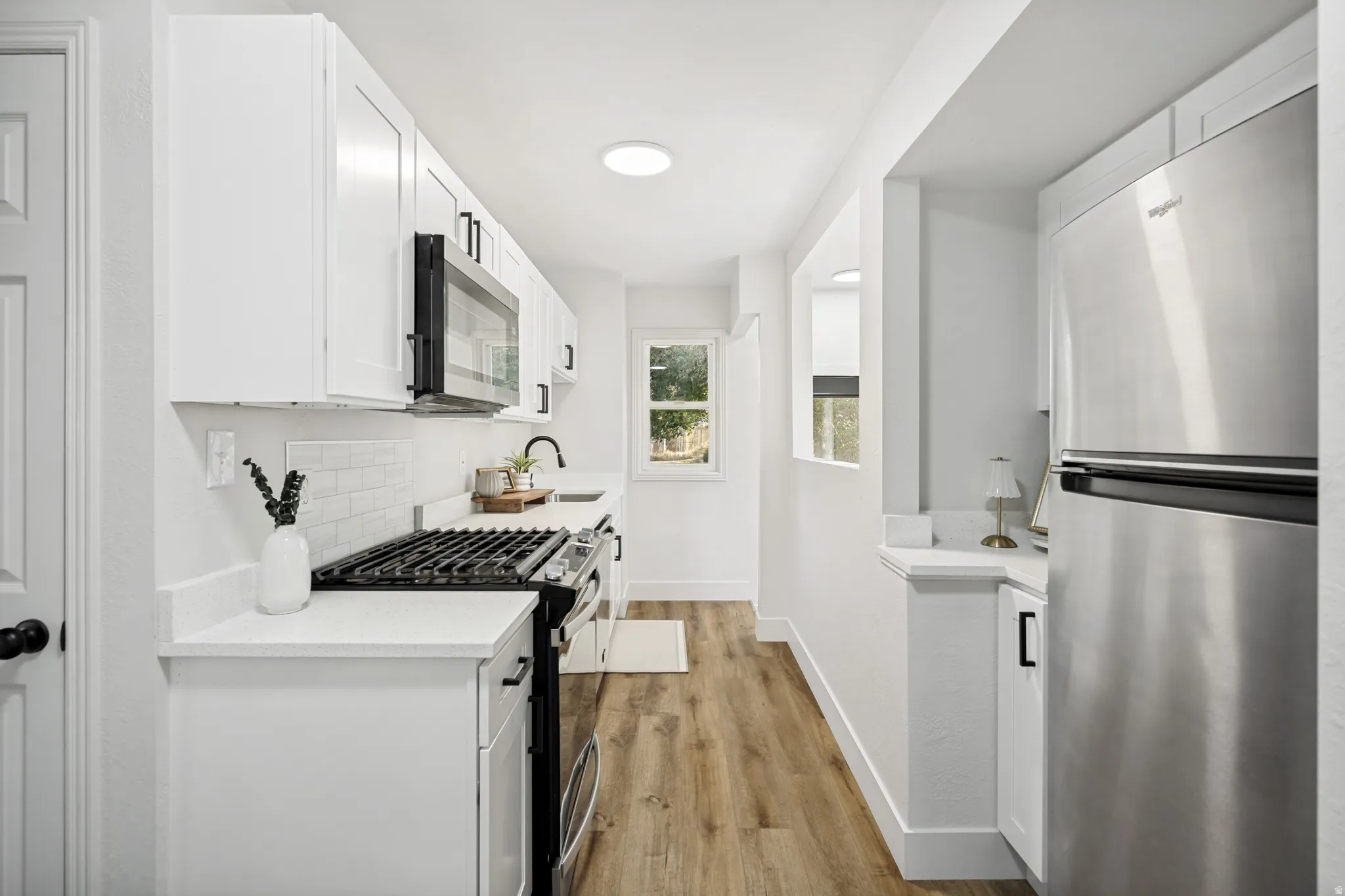 Contemporary kitchen featuring white cabinetry, subway tile backsplash, stone-finish countertops, stainless steel appliances, and wood-finish flooring