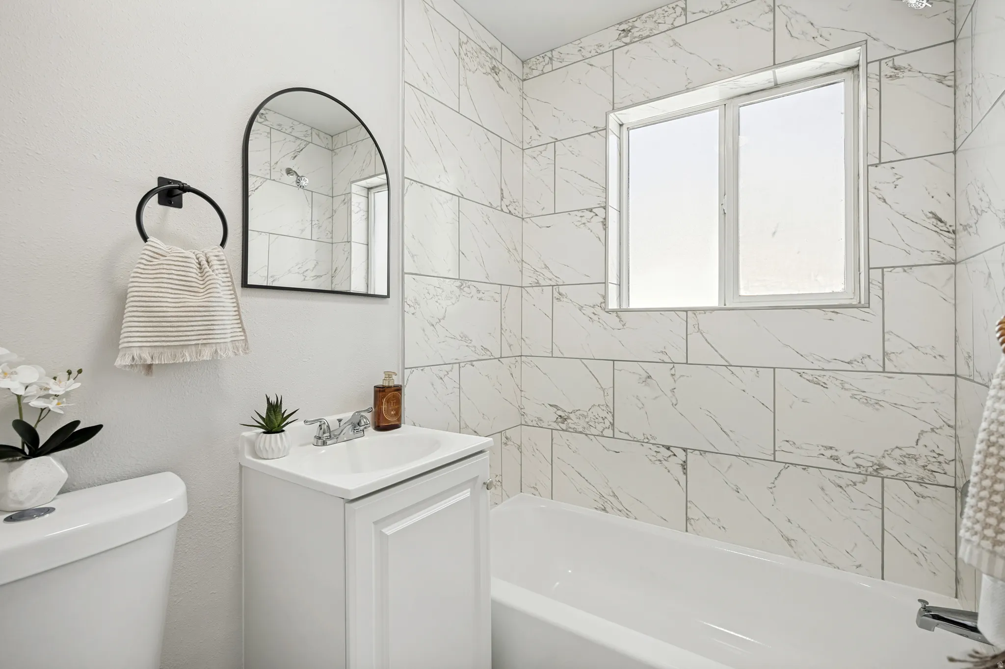 Bathroom featuring a white vanity with a single basin sink, an arched black-framed mirror, and a full bathtub with white subway tile surround