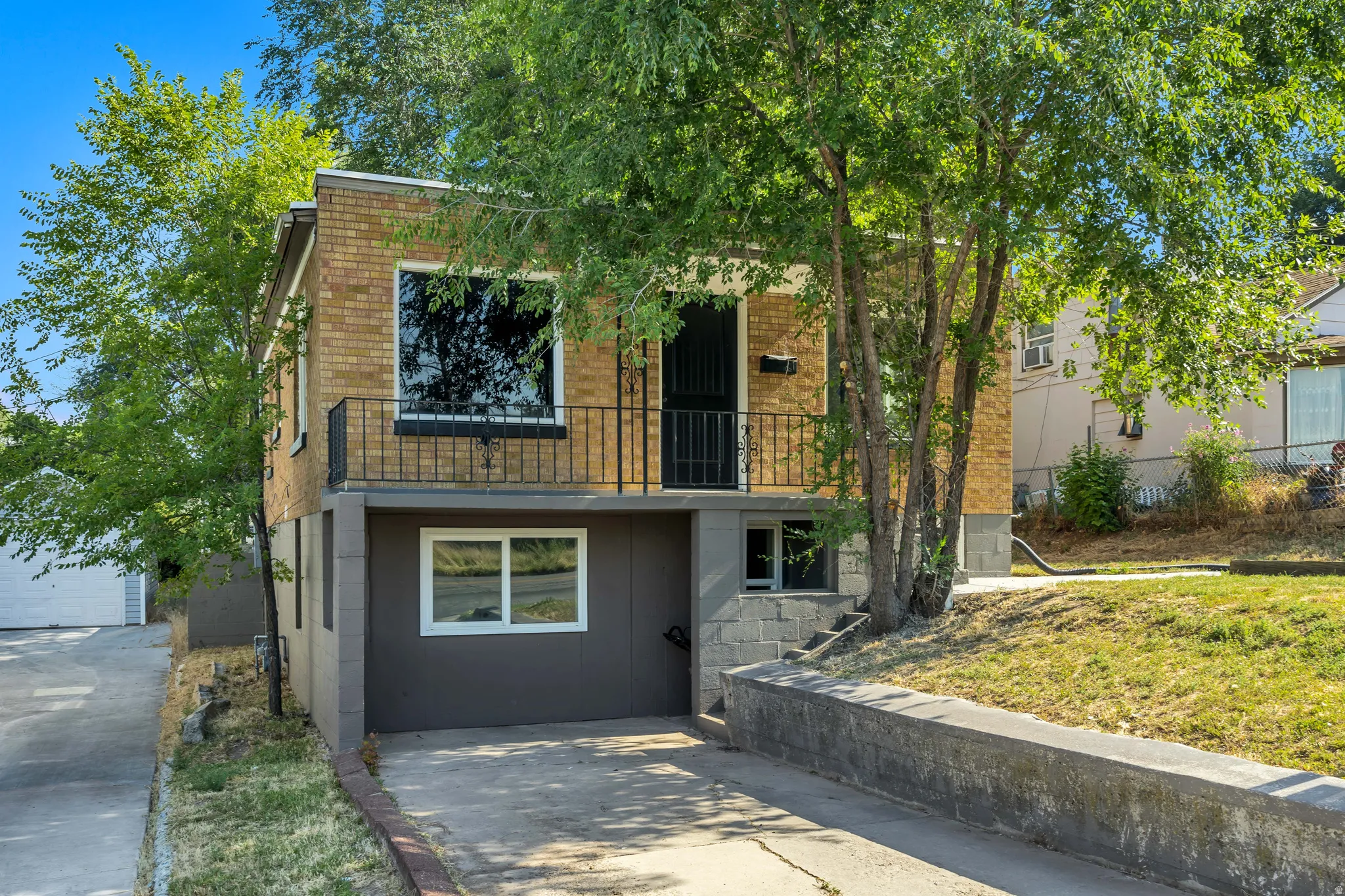 Brick facade residence featuring a balcony with iron railing, lower-level windows, and a paved driveway