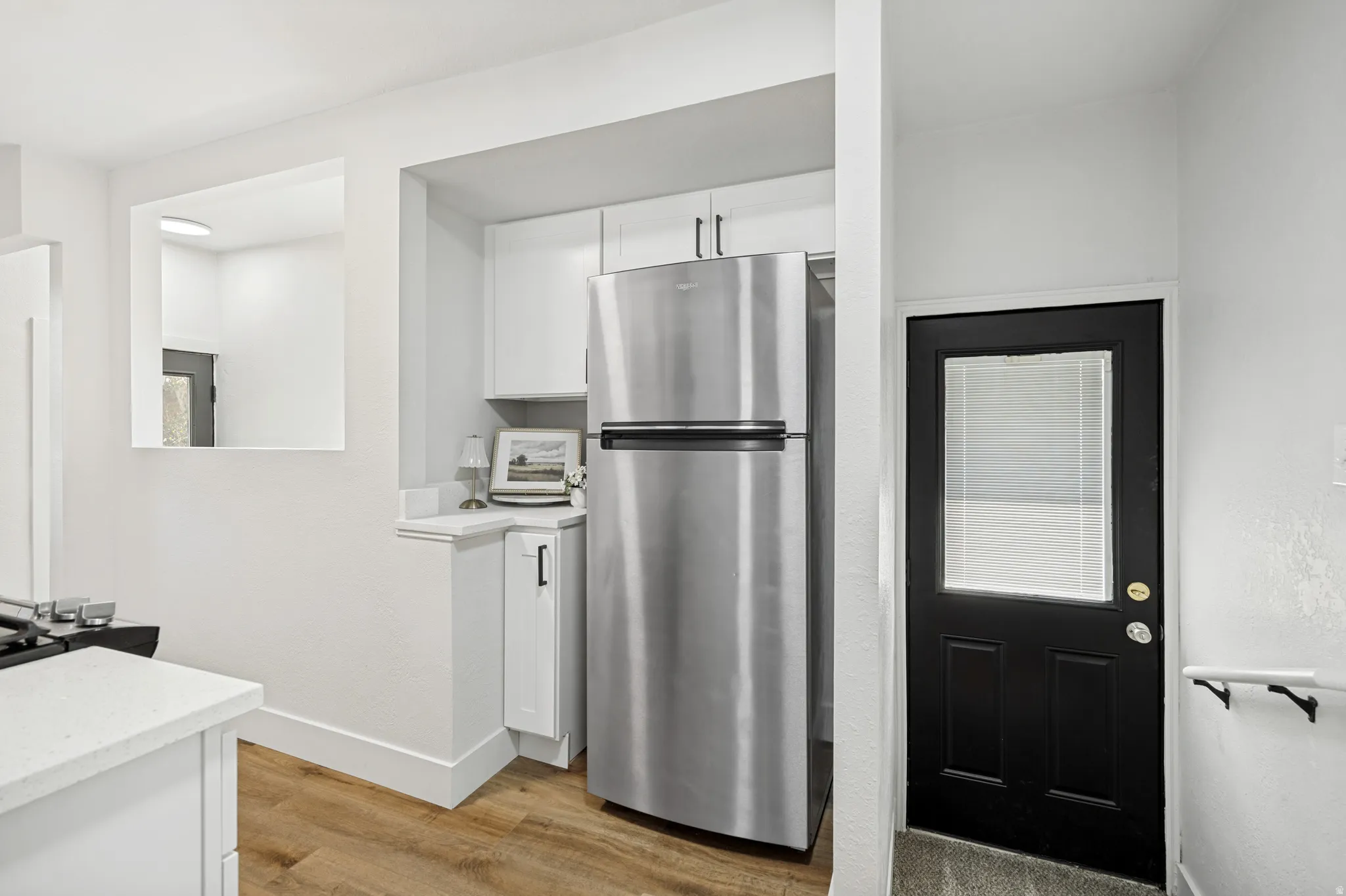 Kitchen area featuring a stainless steel refrigerator, white cabinetry with dark hardware, and wood-finish flooring