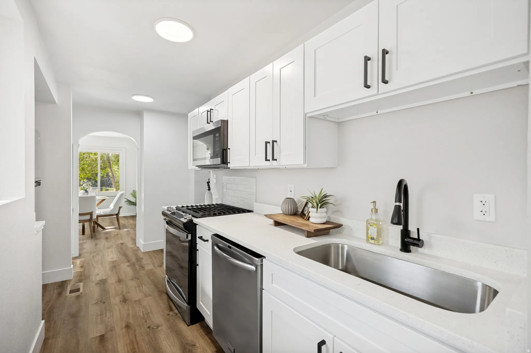 Contemporary kitchen featuring white shaker cabinetry with matte black hardware, stainless steel appliances, a single basin undermount sink with a black gooseneck faucet, and light-toned countertops