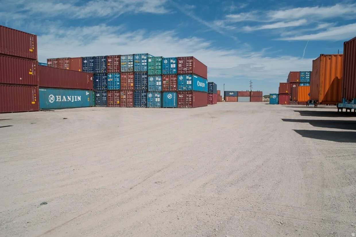 Expansive gravel lot with multiple stacked shipping containers in various colors, providing substantial storage capacity