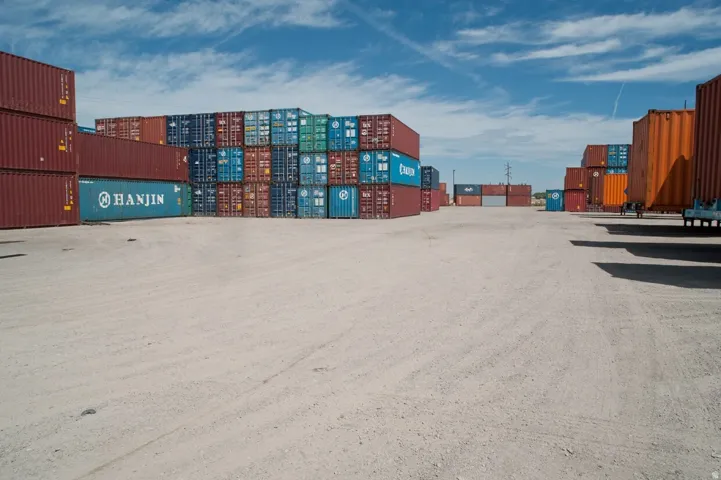 Expansive gravel lot with multiple stacked shipping containers in various colors, providing substantial storage capacity