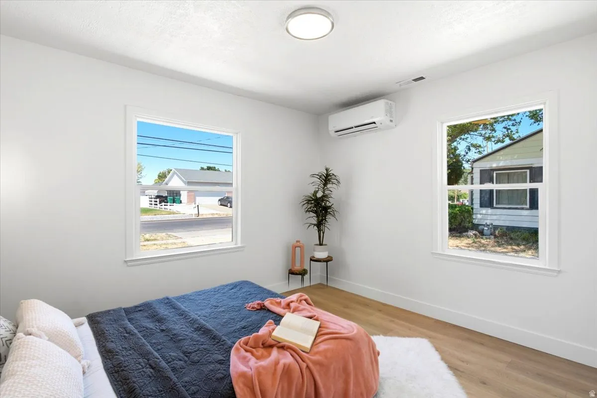 Bright interior space featuring two large windows with white trim, wood-finish flooring, a wall-mounted mini-split system, and a flush-mount ceiling light